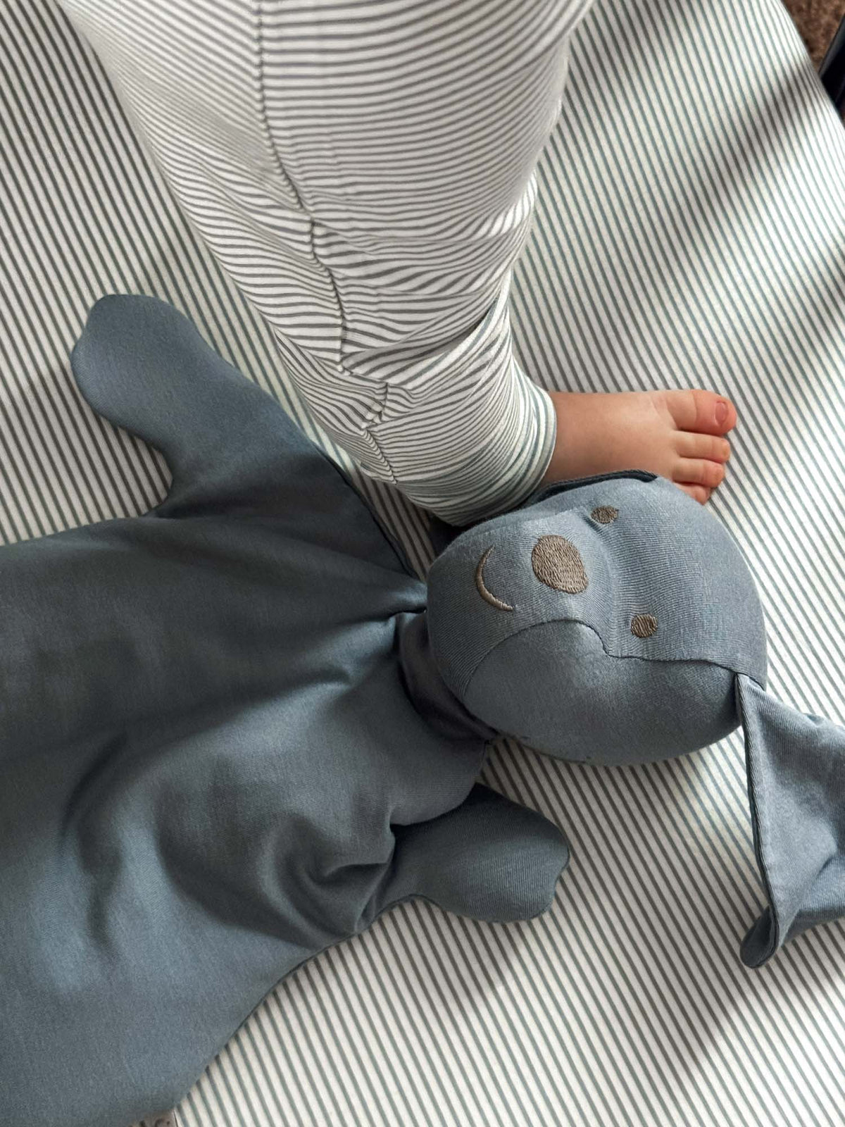Dusky blue plush pup head lovey with embroidered eyes and paws on striped blanket