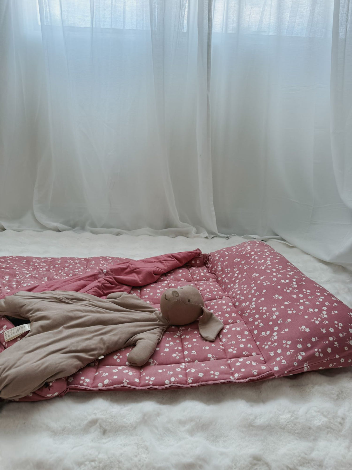 Taupe puppy plush lovey lying on a pink and white speckled comforter.
