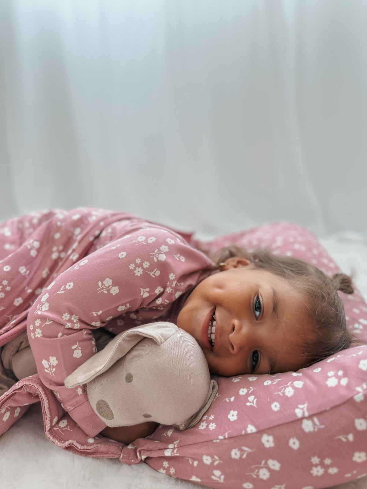 Baby cuddling taupe puppy plush lovey on a pink patterned blanket.