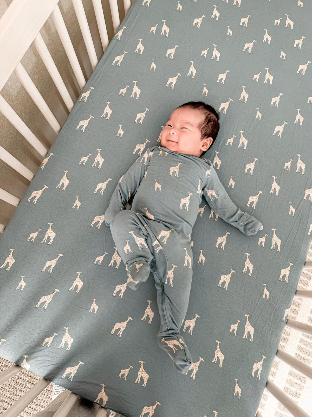 Crib sheet with teal fabric and repeating giraffe pattern, baby lying down