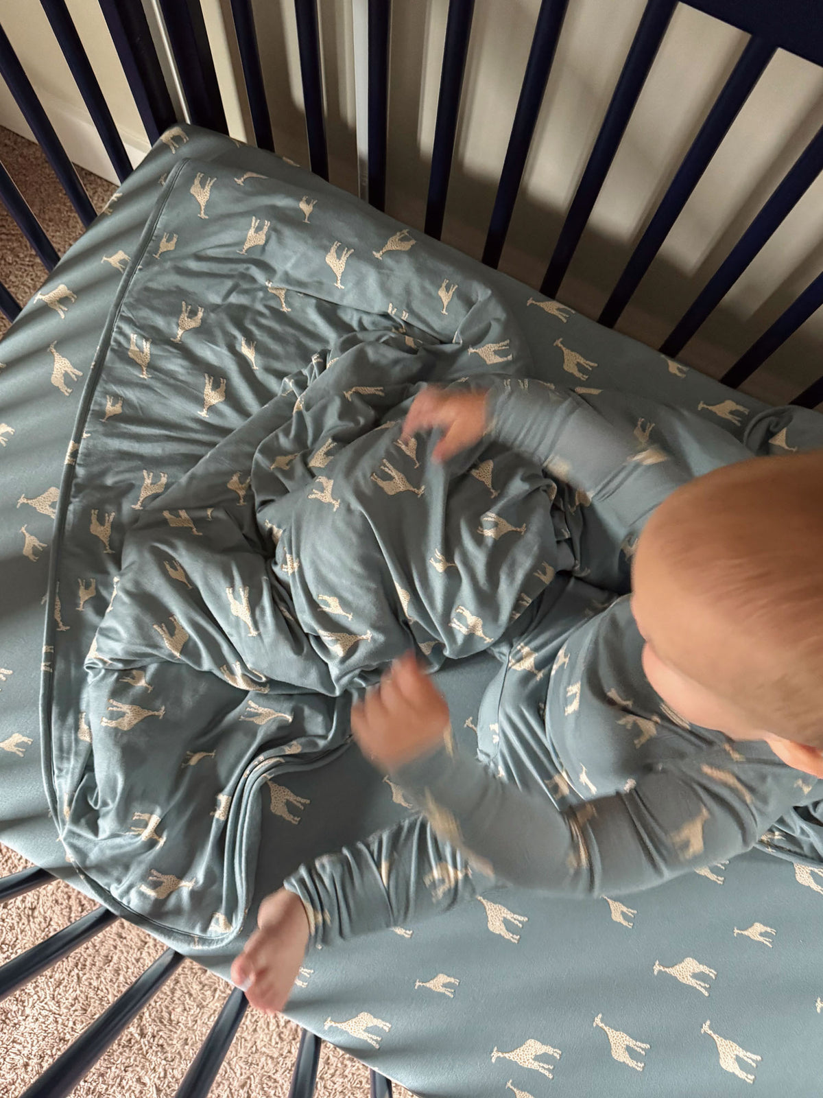 Teal crib sheet with beige giraffe pattern spread on crib frame, corner creases