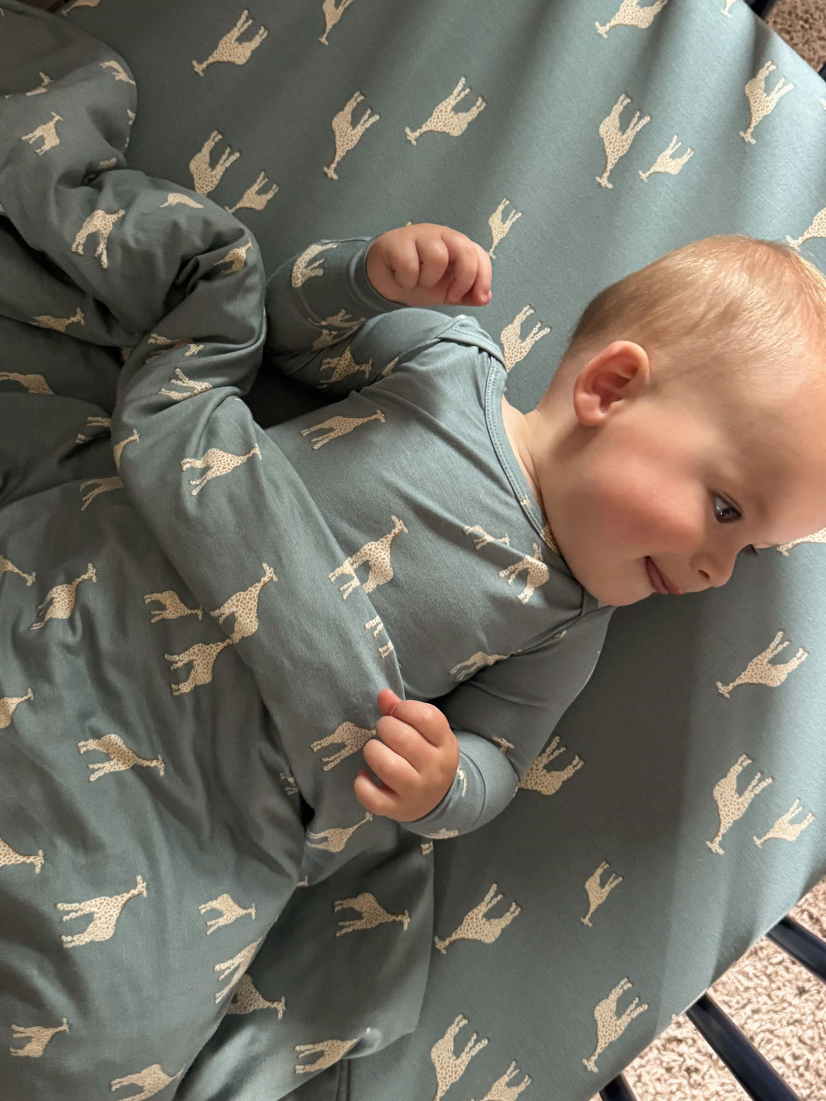 Baby on teal crib sheet with beige giraffe print, close view of toddler