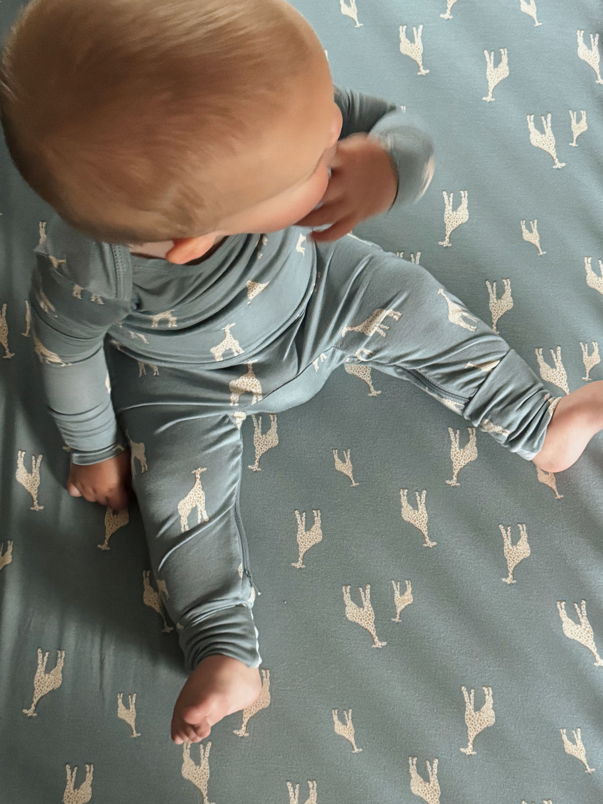 Crib sheet in teal with beige giraffe print, baby crawling on the fabric