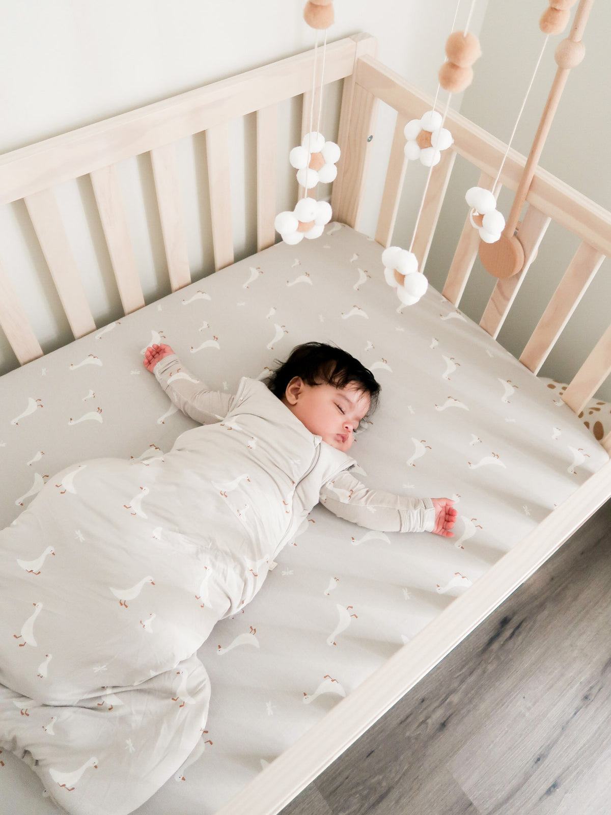 Light taupe crib sheet with small white goose print, fully spread