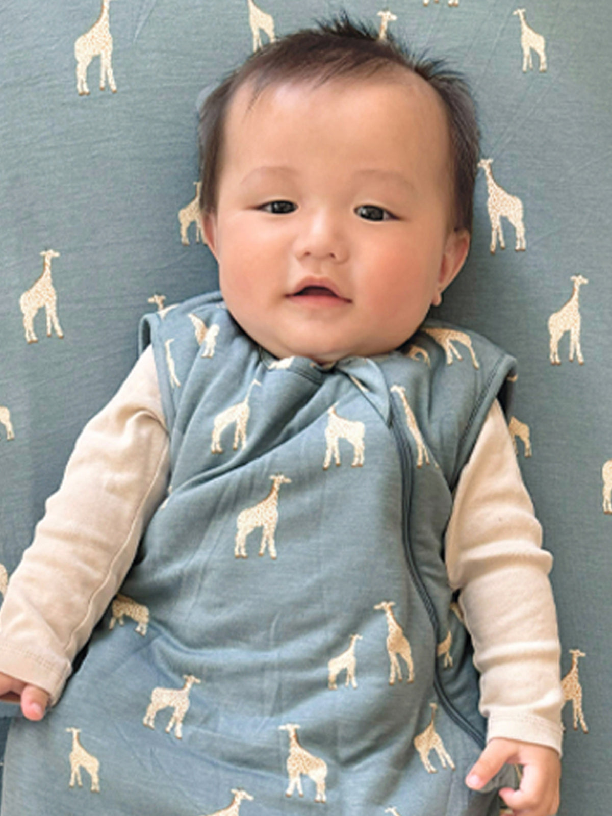 Baby on teal crib sheet with beige giraffe pattern, wearing light pants