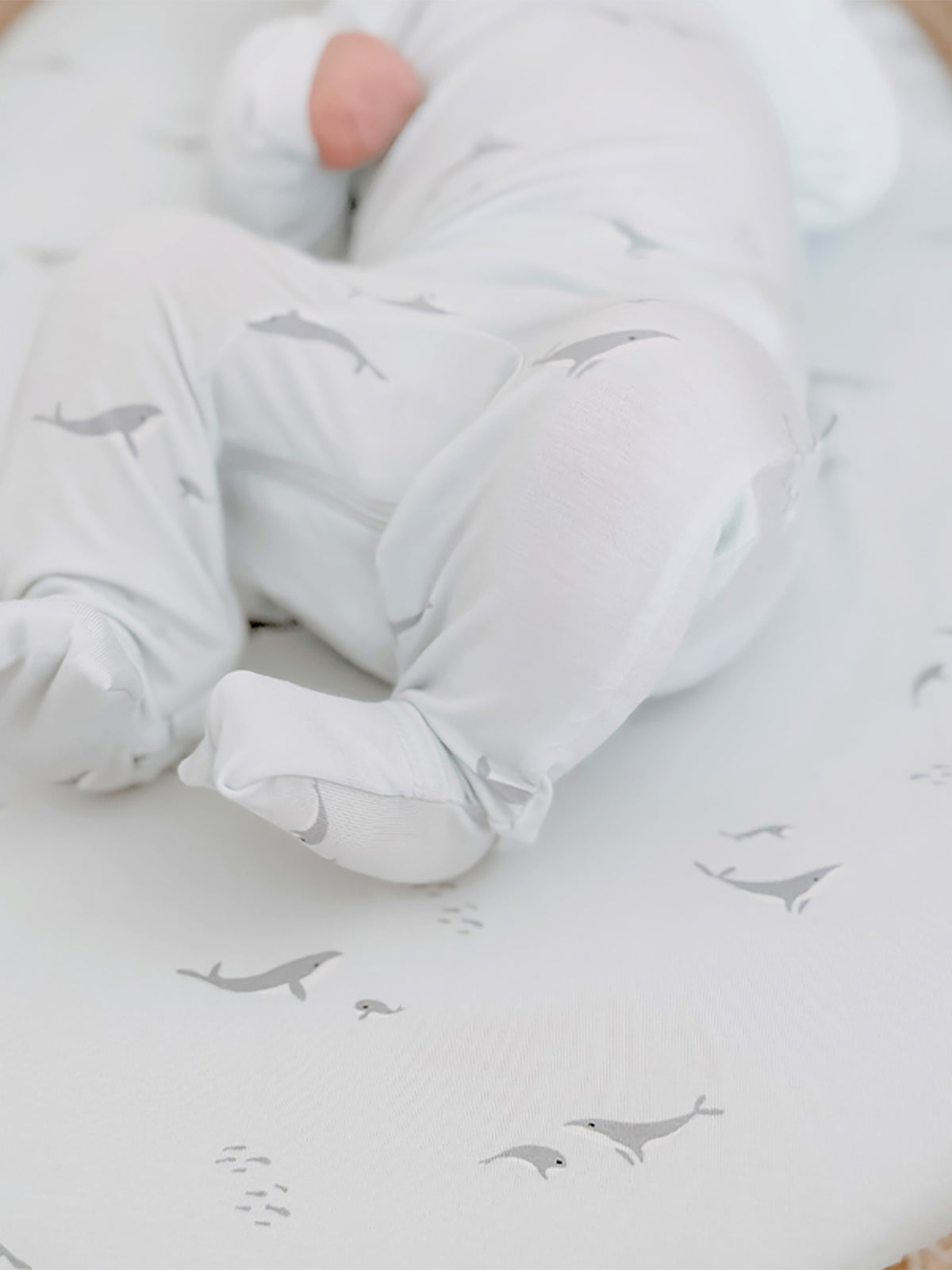 Changing pad cover with gray whale print, baby's swaddled feet visible
