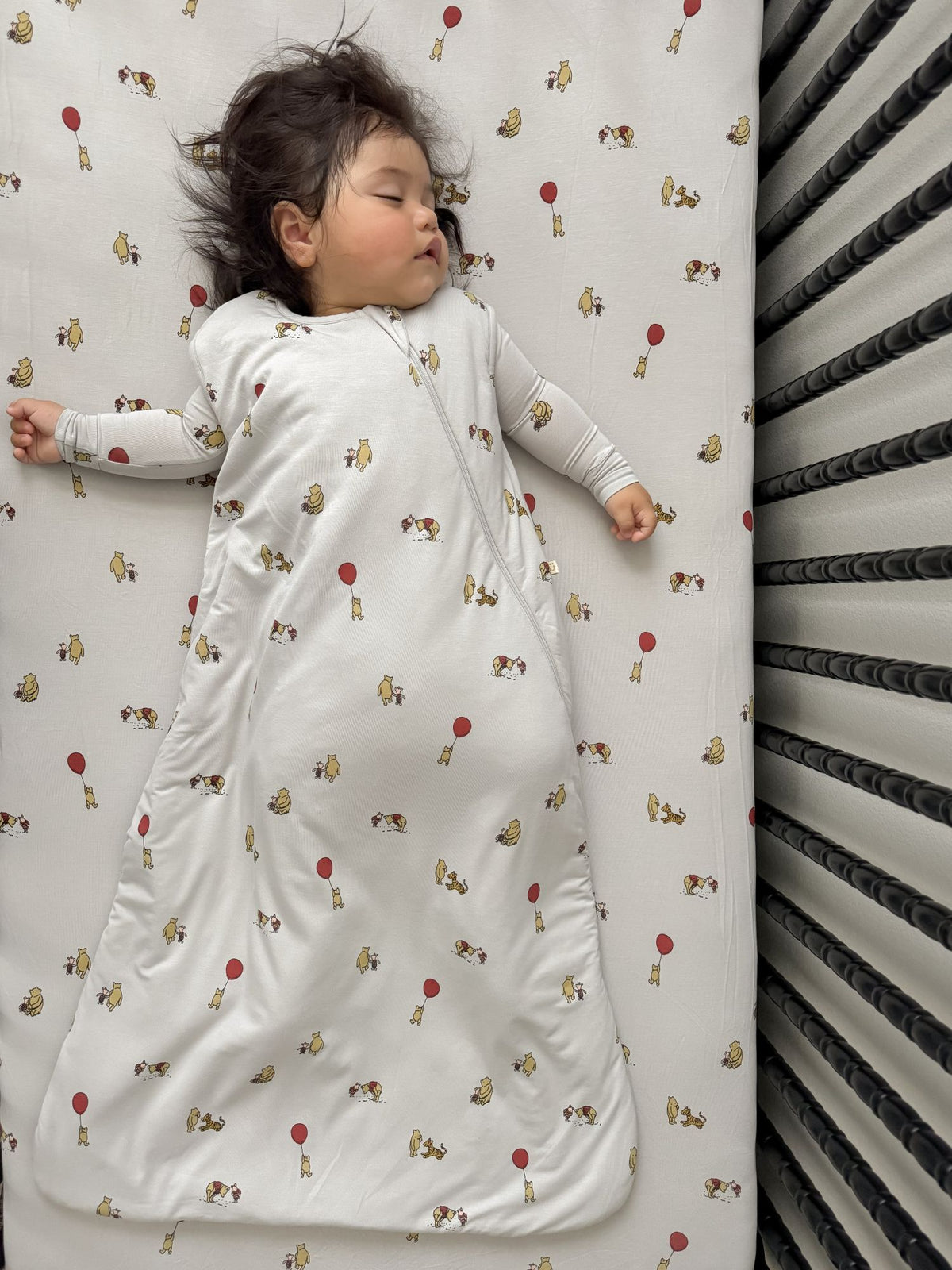 White baby sleep sack with Pooh character print, baby wearing it with open arms