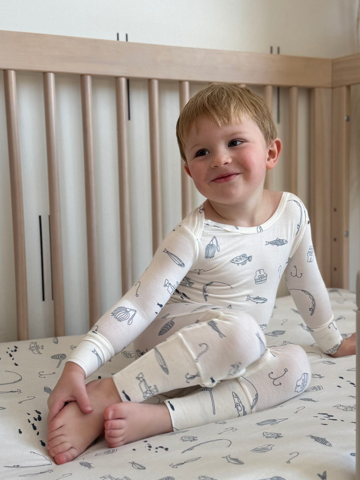 Off-white kids long-sleeve pajama set with fishing-themed print, toddler seated