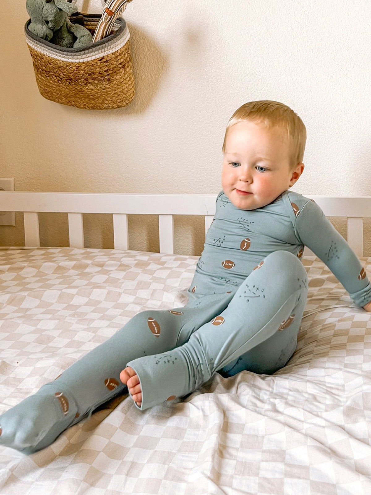 Light blue baby pajamas with football print, toddler sitting with one leg bent