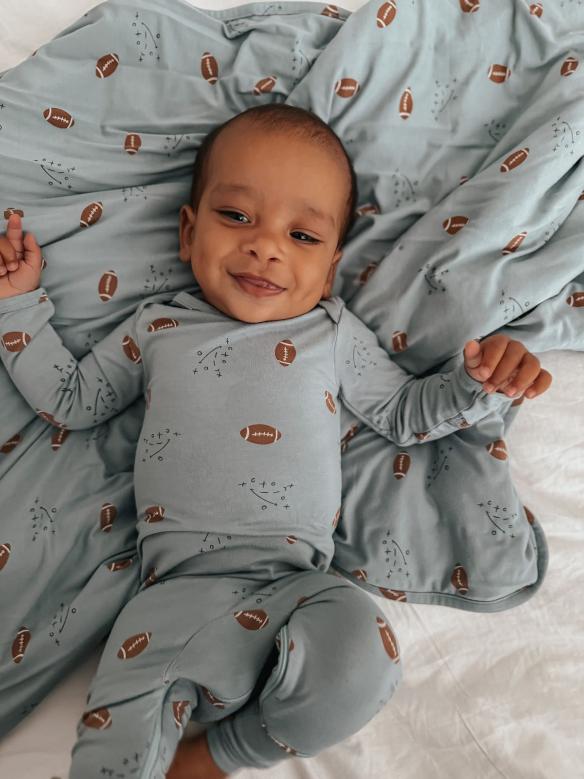 Baby pajamas in light blue with football print and fold-over cuffs; smiling infant