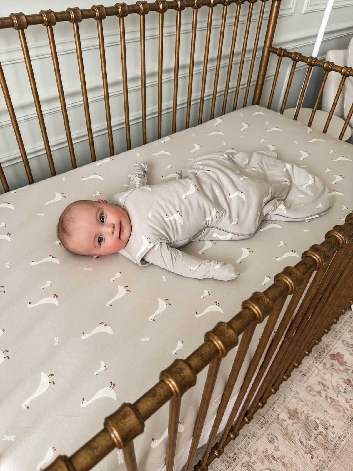 Beige swaddle sleep sack with white goose print on crib mattress
