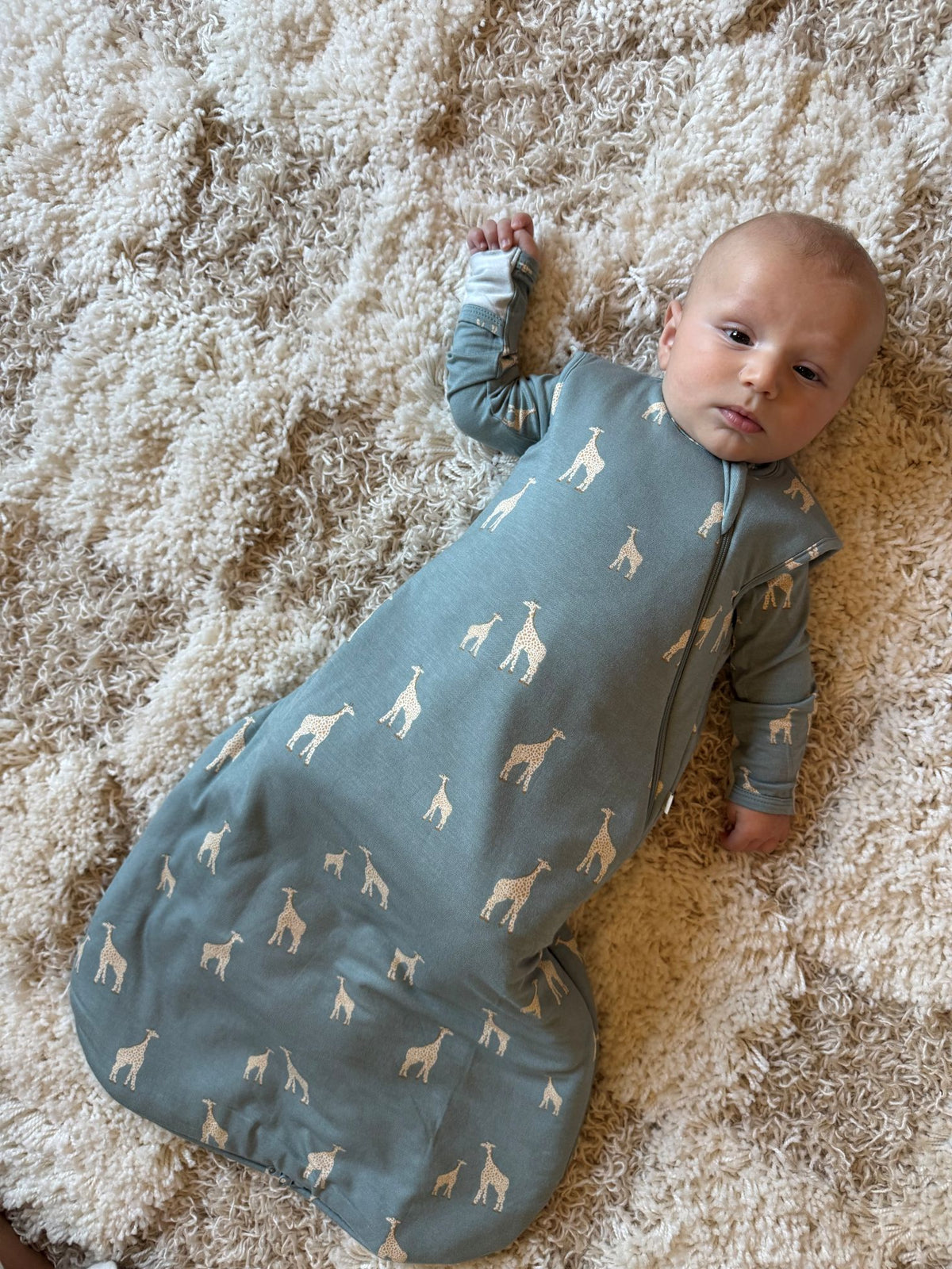 Moss green sleep sack with giraffe print and zip front, laid on a rug
