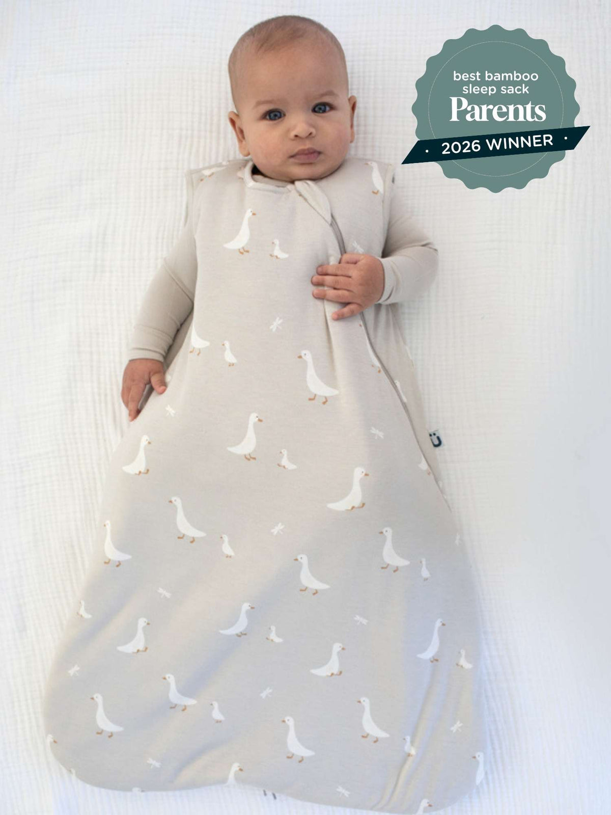 Light gray baby sleep sack with scattered white duck print, worn on a standing baby