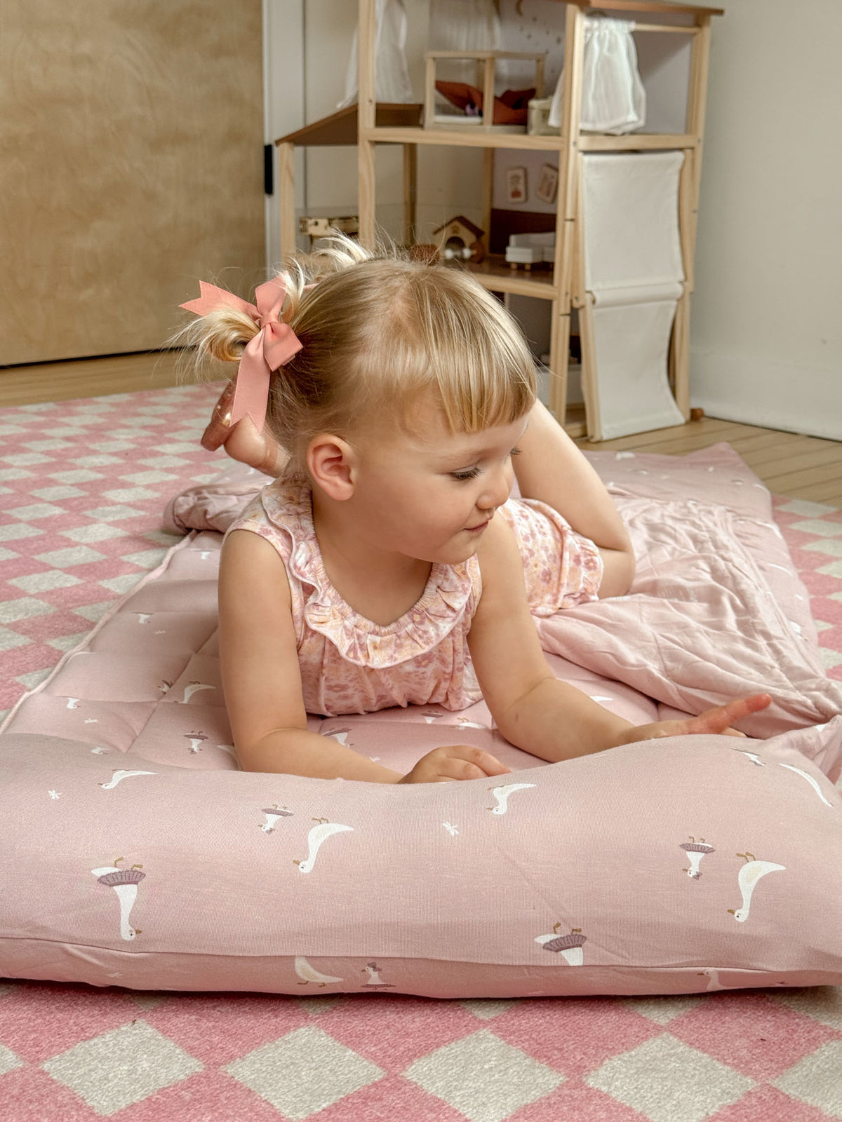 Light pink nap mat with white goose pattern, baby lying on top of the cushion