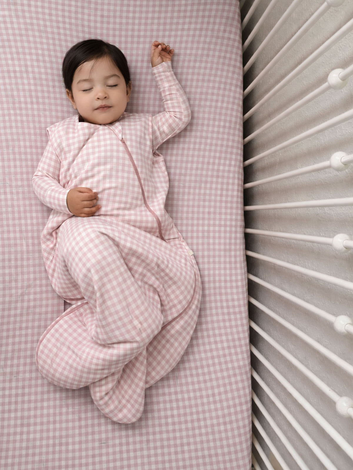 Baby wearing a pink gingham zippered sleep sack with padded quilted panels