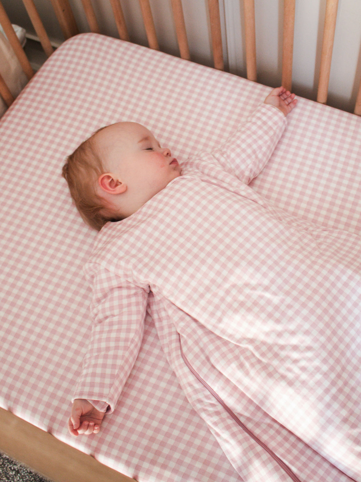 Pink gingham sleep sack with long sleeves and center front zipper, lying on back