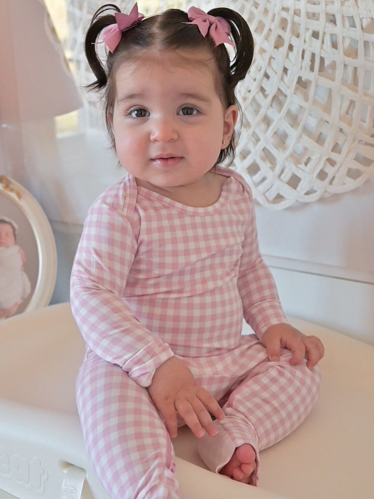 Pink gingham long-sleeve pajama romper on baby with rounded neckline