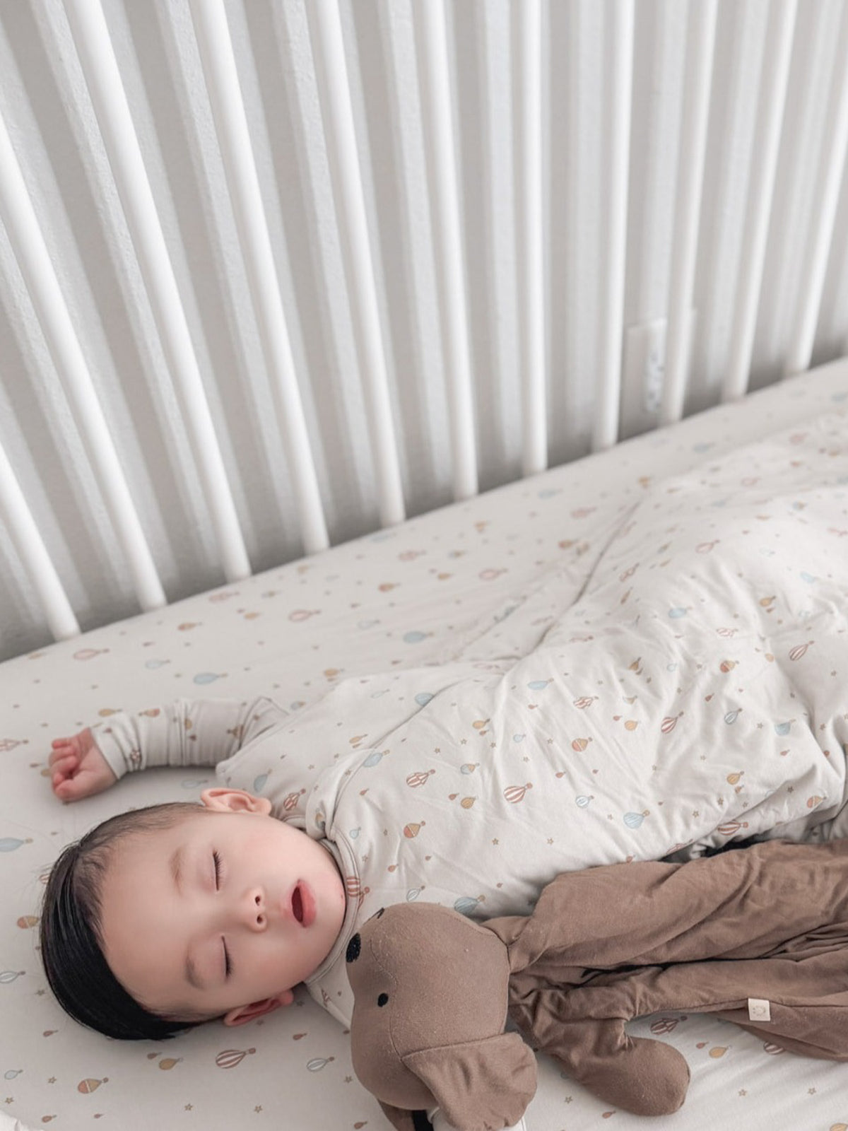 Cream 1.0 TOG sleep sack with multicolor planet print, worn by baby lying down