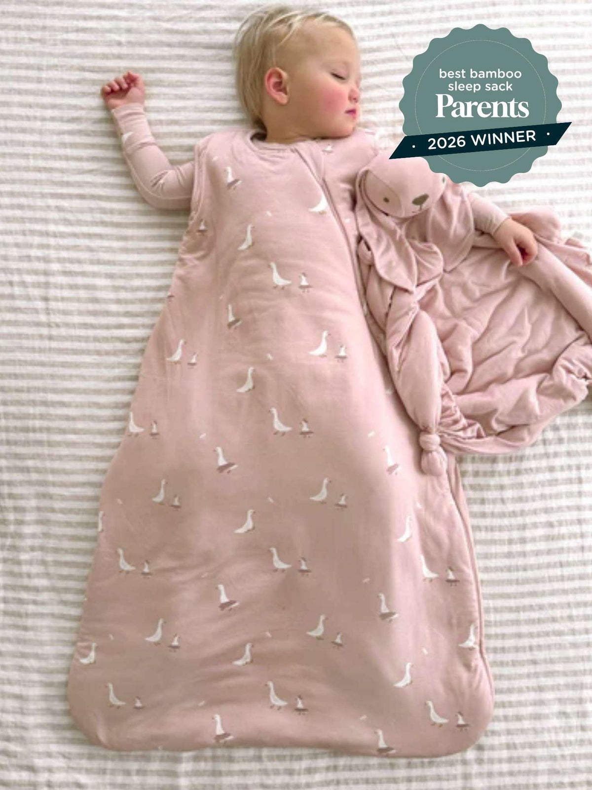 Blush pink sleep sack with white swan print, baby lying on back with arms up
