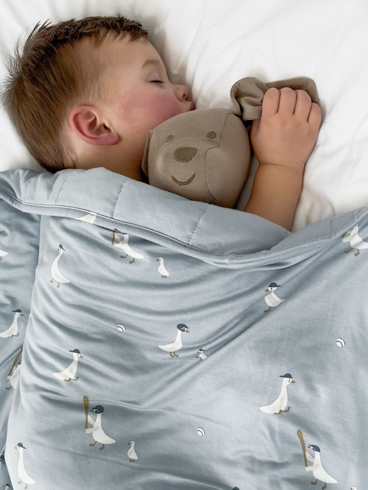 Light blue goose-print baby blanket with teddy plush next to child