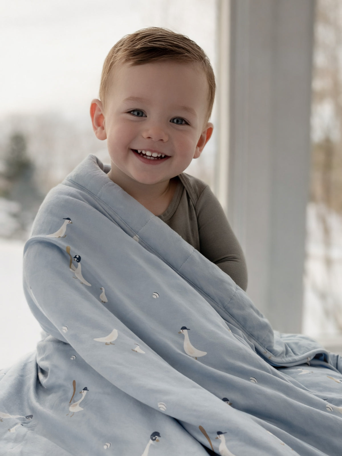 Light blue baby blanket with white goose print, draped over smiling child
