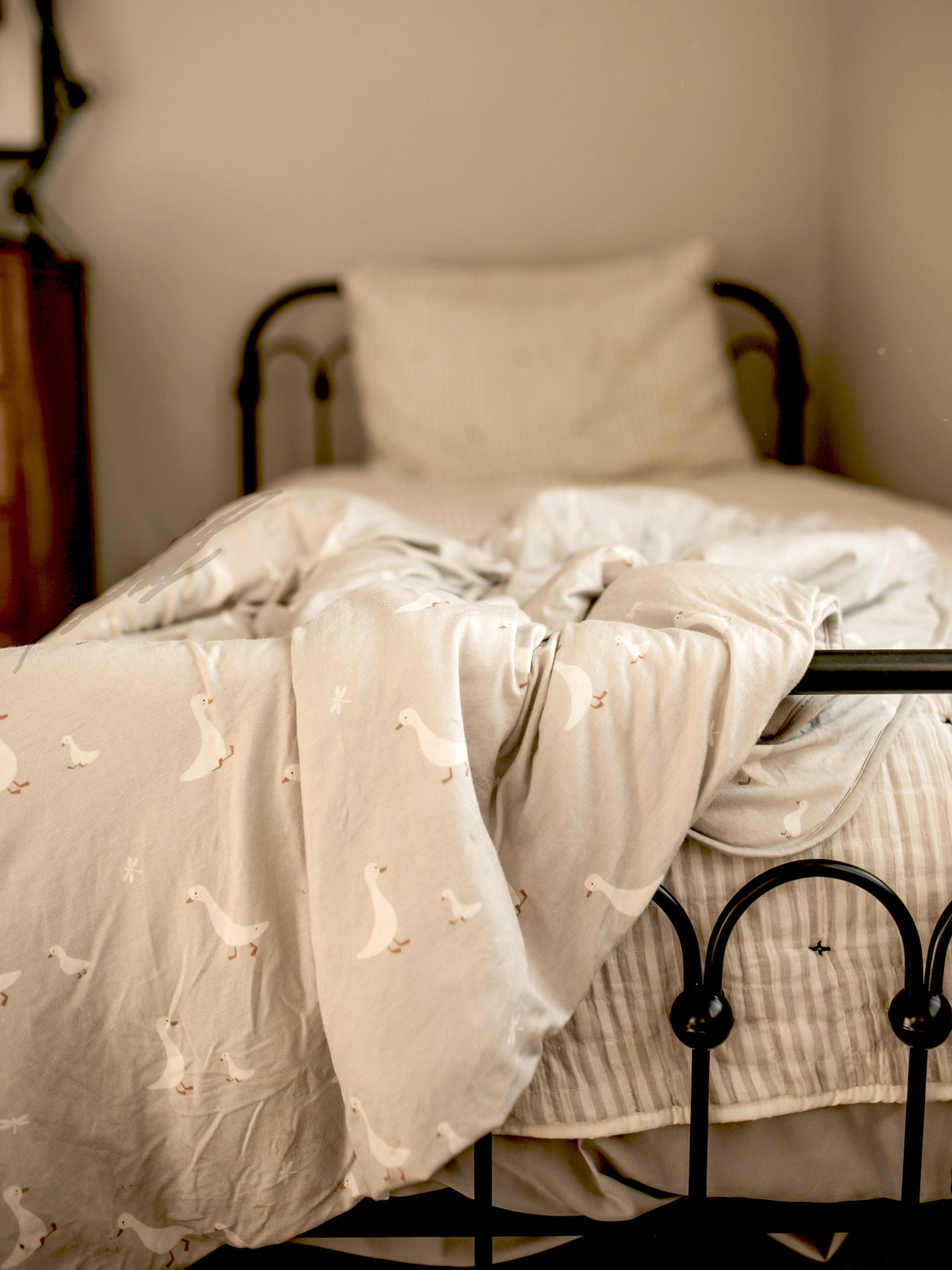 Light gray duvet-style blanket with small white goose print, folded over bed.