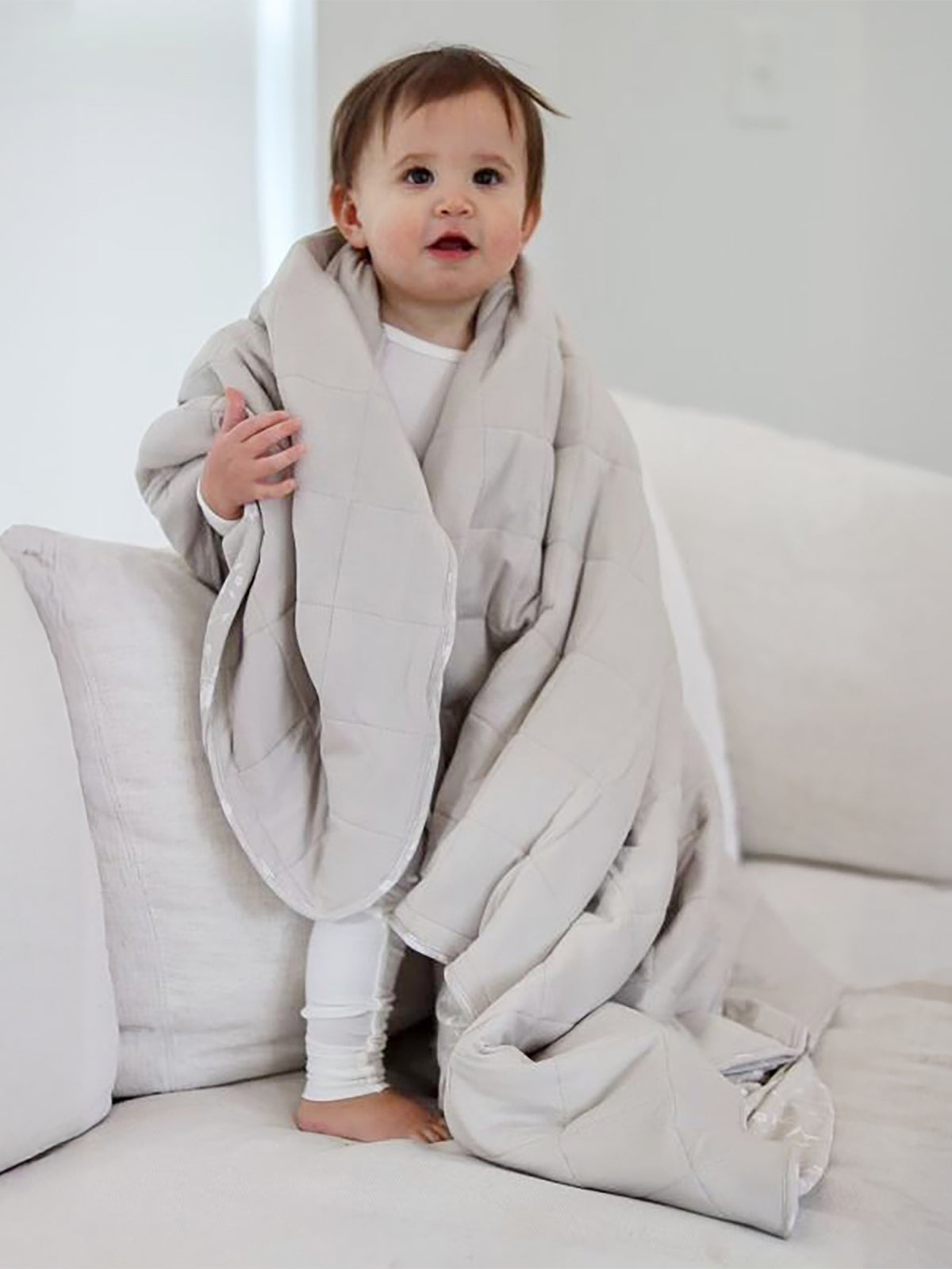Light beige baby cloud blanket with quilted wave pattern, draped on a sofa