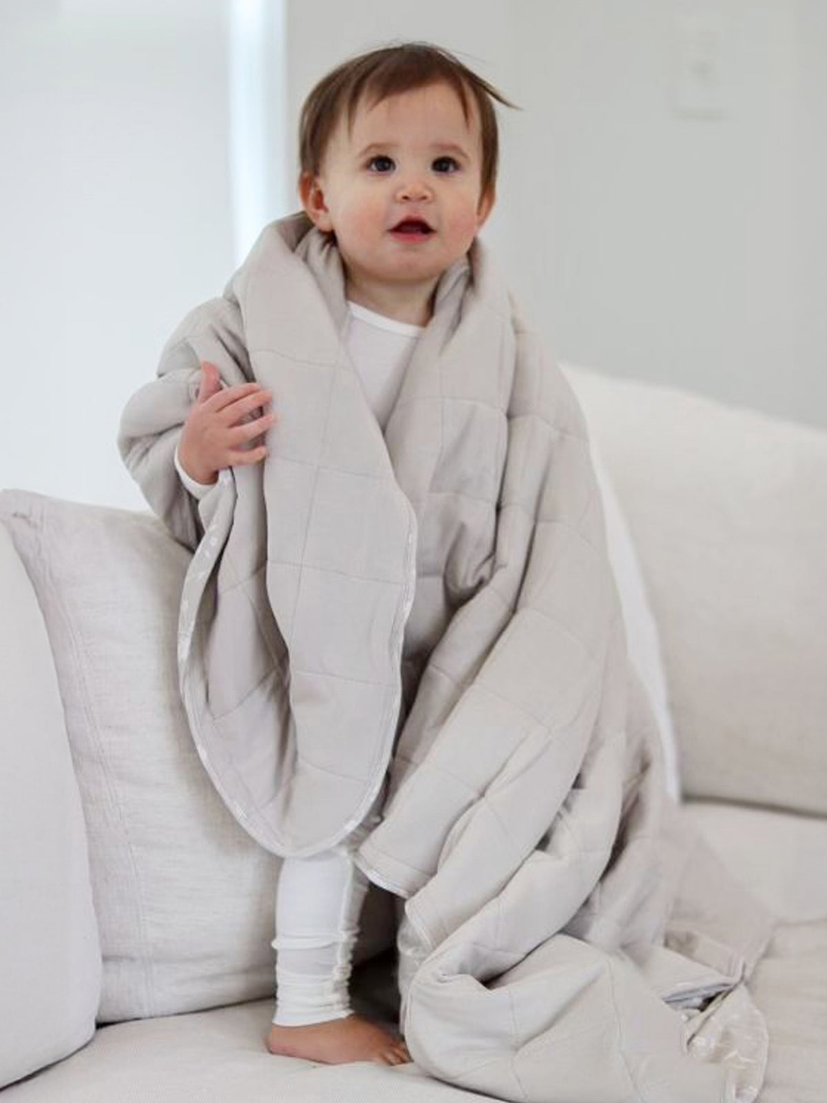 Light gray quilted baby blanket draped over shoulders, soft cloud-style stitching
