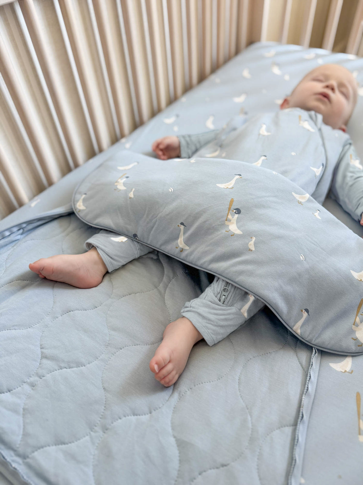 Light blue sleep sack with white goose print, partially covering baby on bed