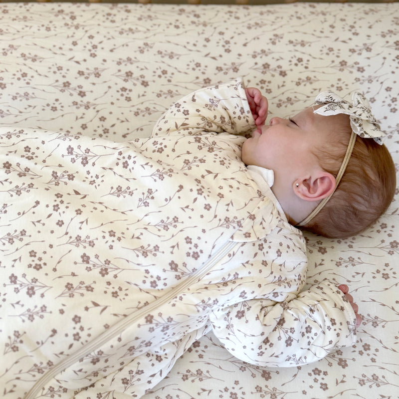 Infant long-sleeve sleep sack in cream with tiny floral print, baby lying on back
