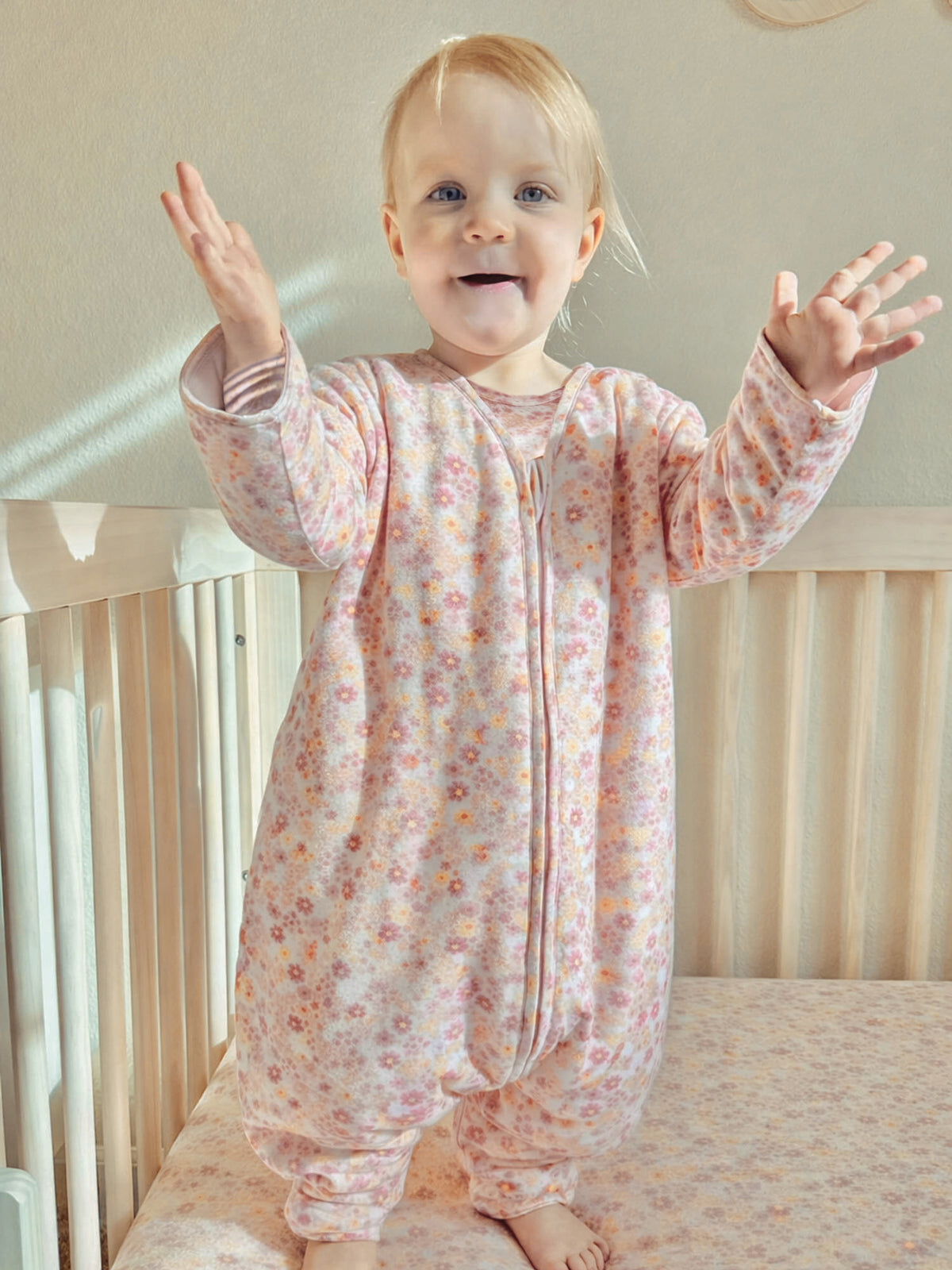 Long-sleeve footed sleep sack with pastel floral print, zip front, standing pose