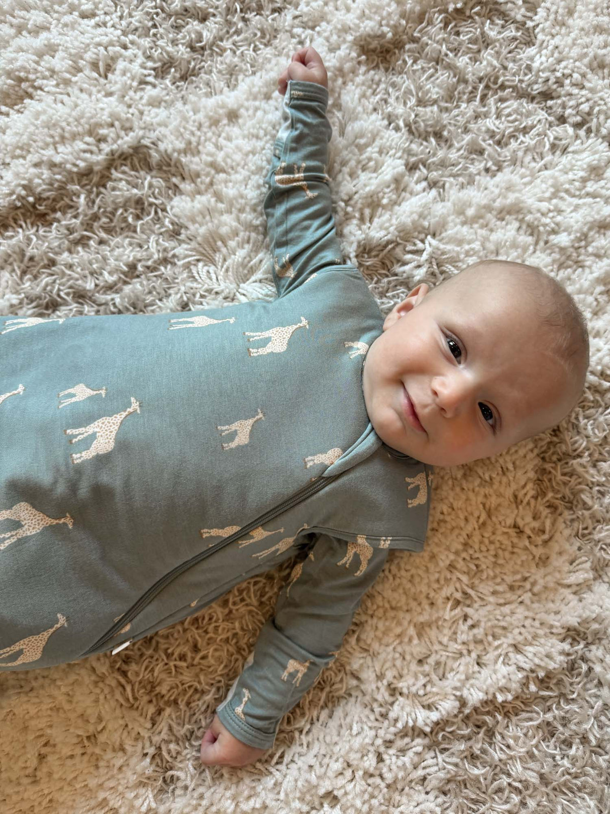 Moss green swaddle sleep sack with giraffe print, zip front, on a rug