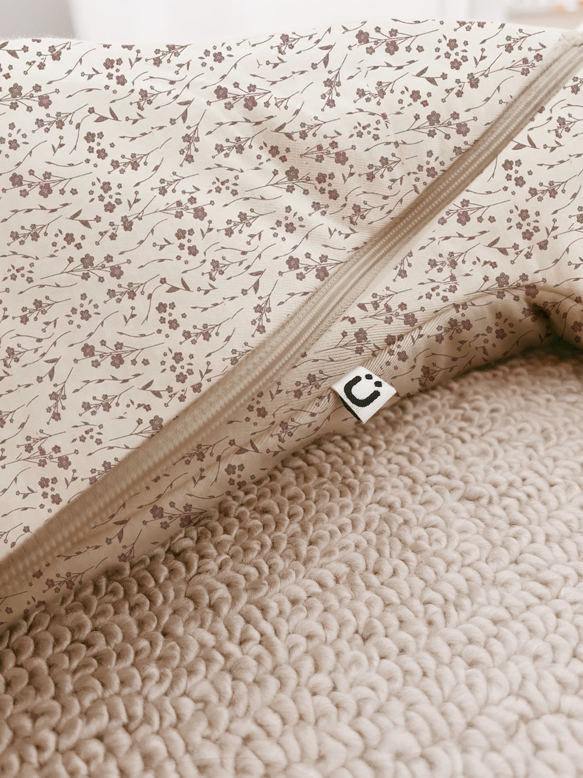 Beige fabric close-up of 1.0 TOG swaddle sack zipper track and stitched edge tag