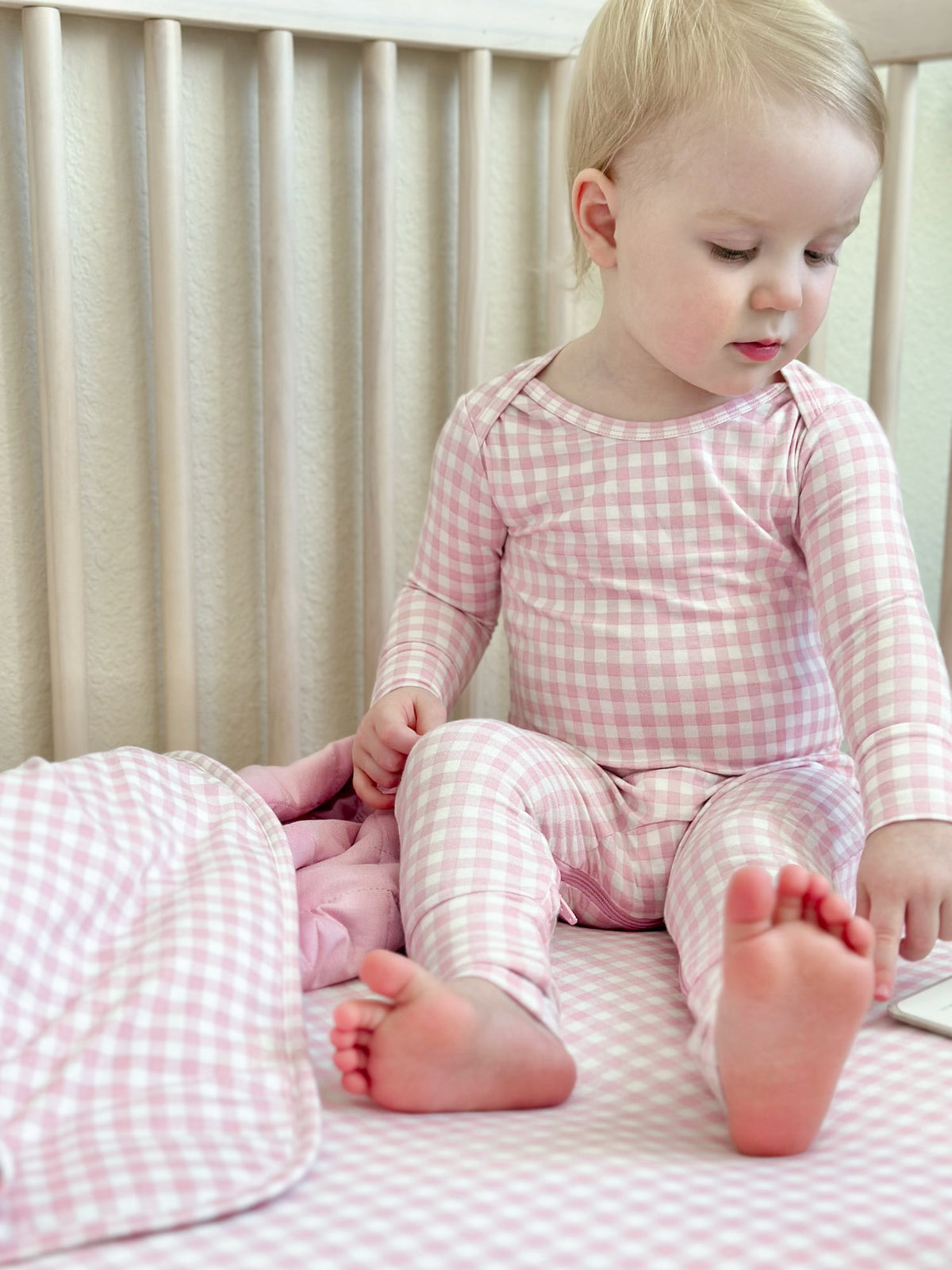 Pink gingham baby pajama set with long sleeves and footed bottoms, sitting pose
