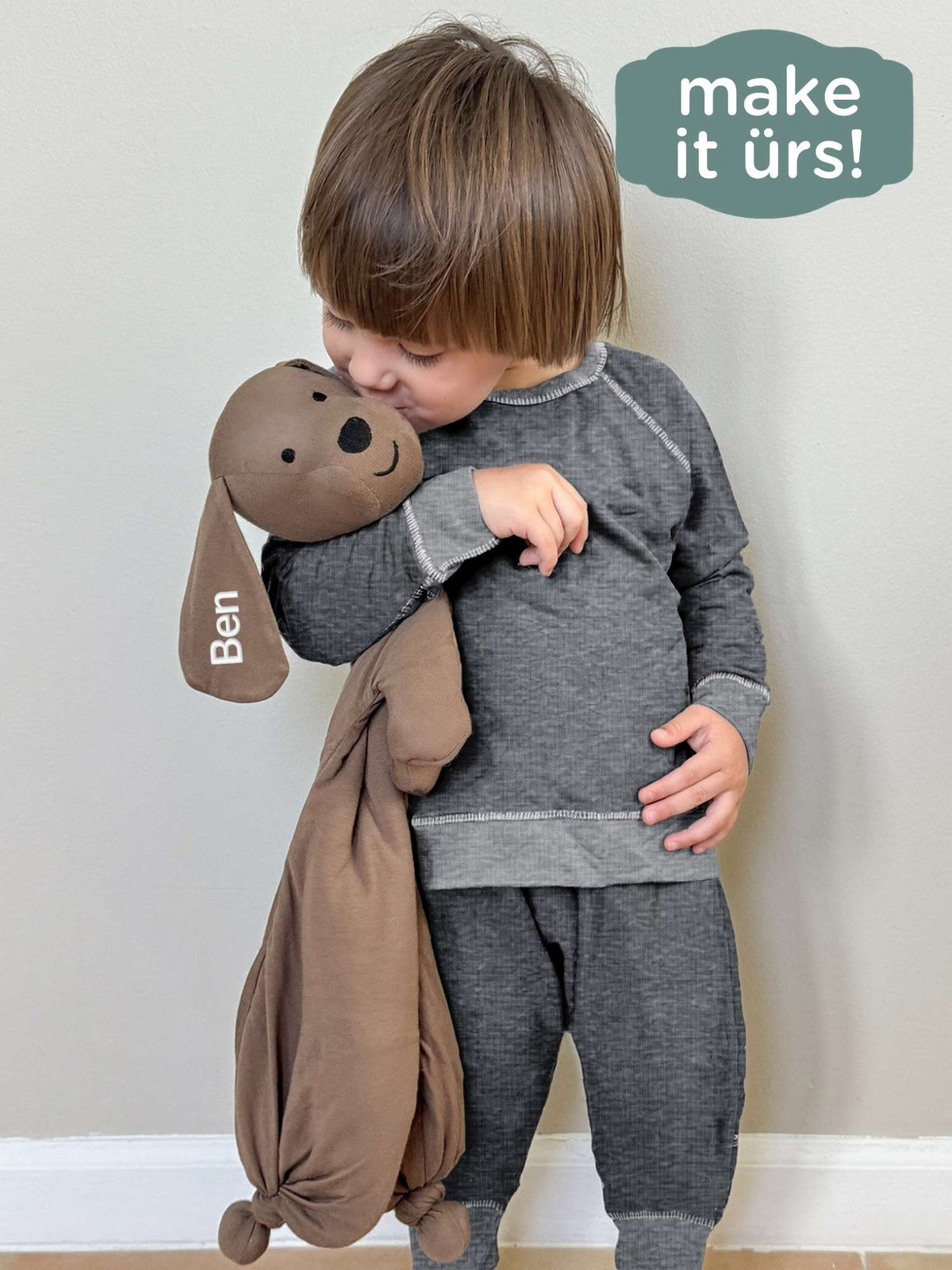 Plush dog lovey with floppy ears and stitched face, held against baby's torso.