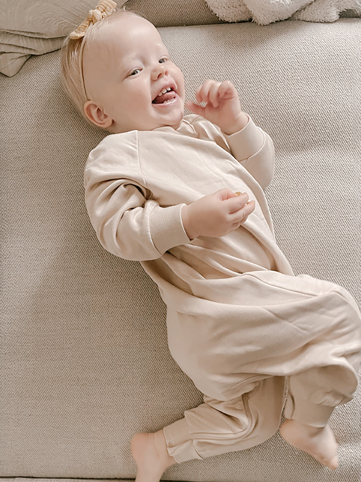 Blush fleece baby jumpsuit with long sleeves and footed legs, worn on sofa