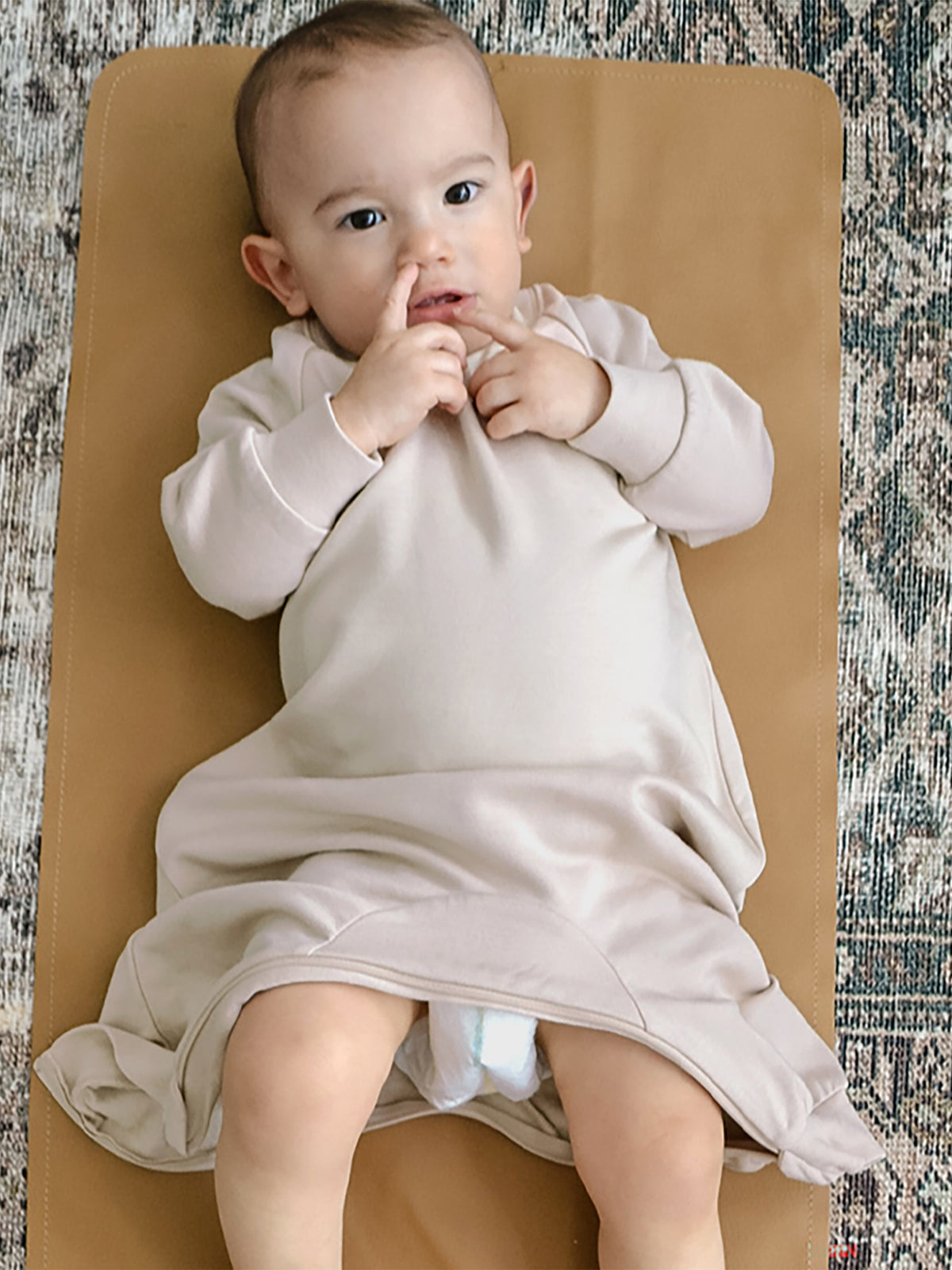 Blush fleece baby jumpsuit with long sleeves, sitting with hands near mouth