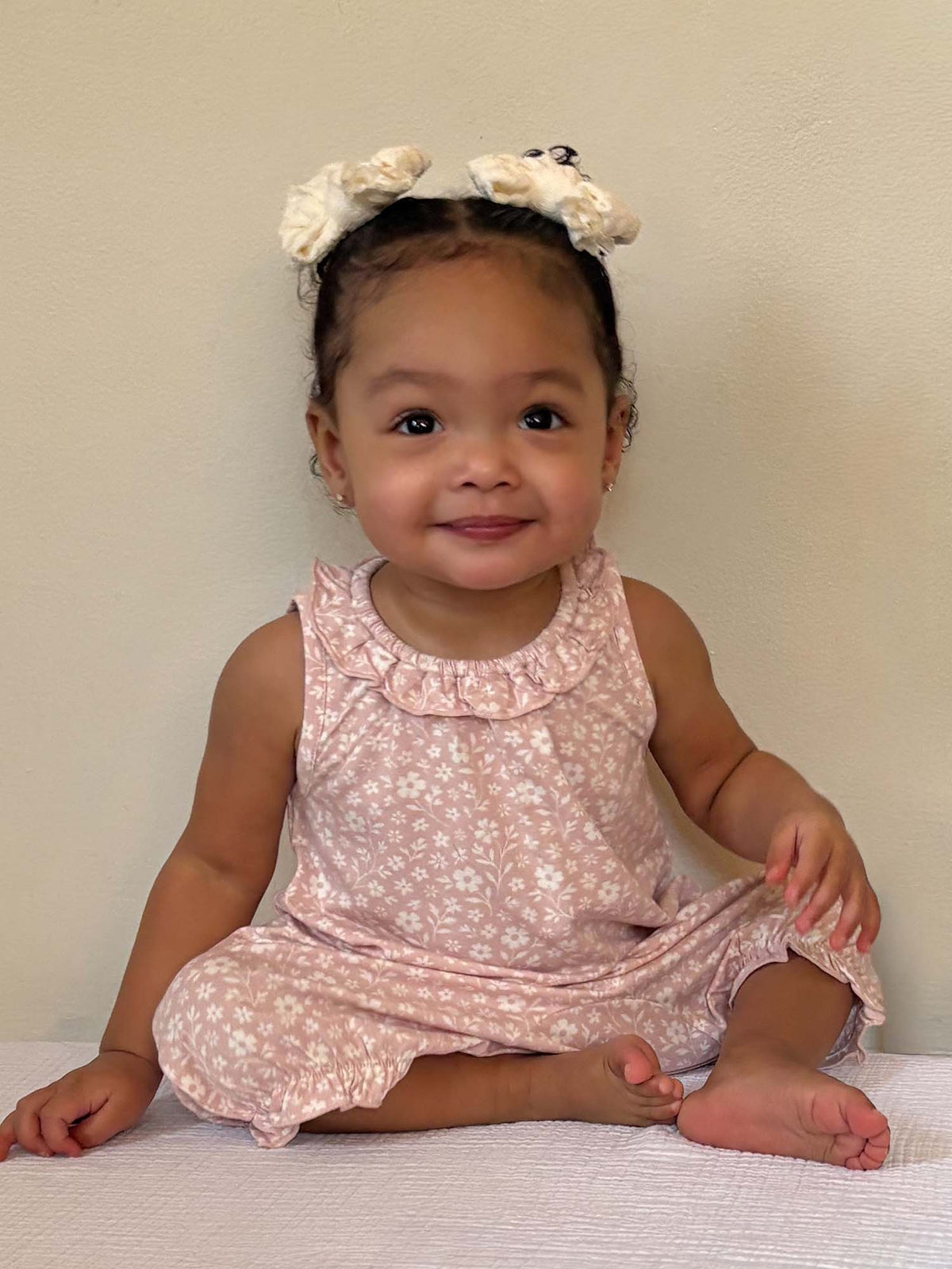 Light pink floral bubble romper with ruffled neckline, baby sitting and smiling