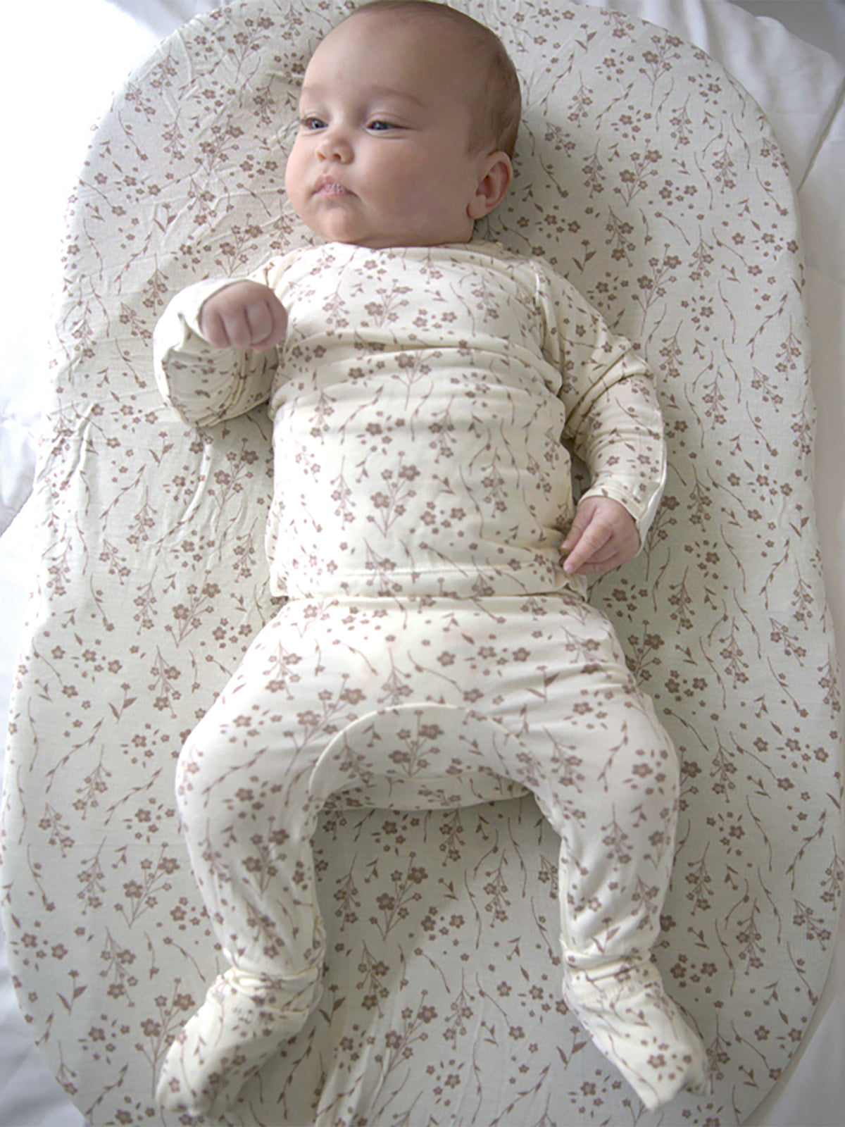 Cream floral footie pajamas with long sleeves and gathered waist; baby standing