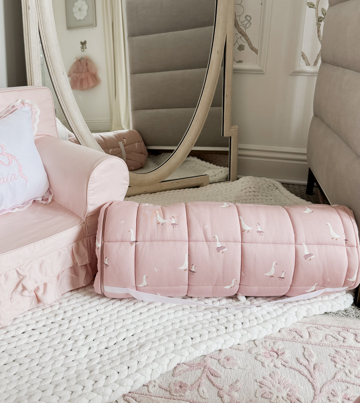 Light pink nap mat with white goose pattern, padded sides and fold-over bolster