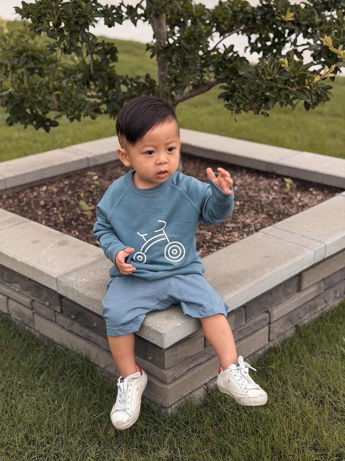 Kids blue crewneck sweatshirt with white bike graphic, worn with shorts