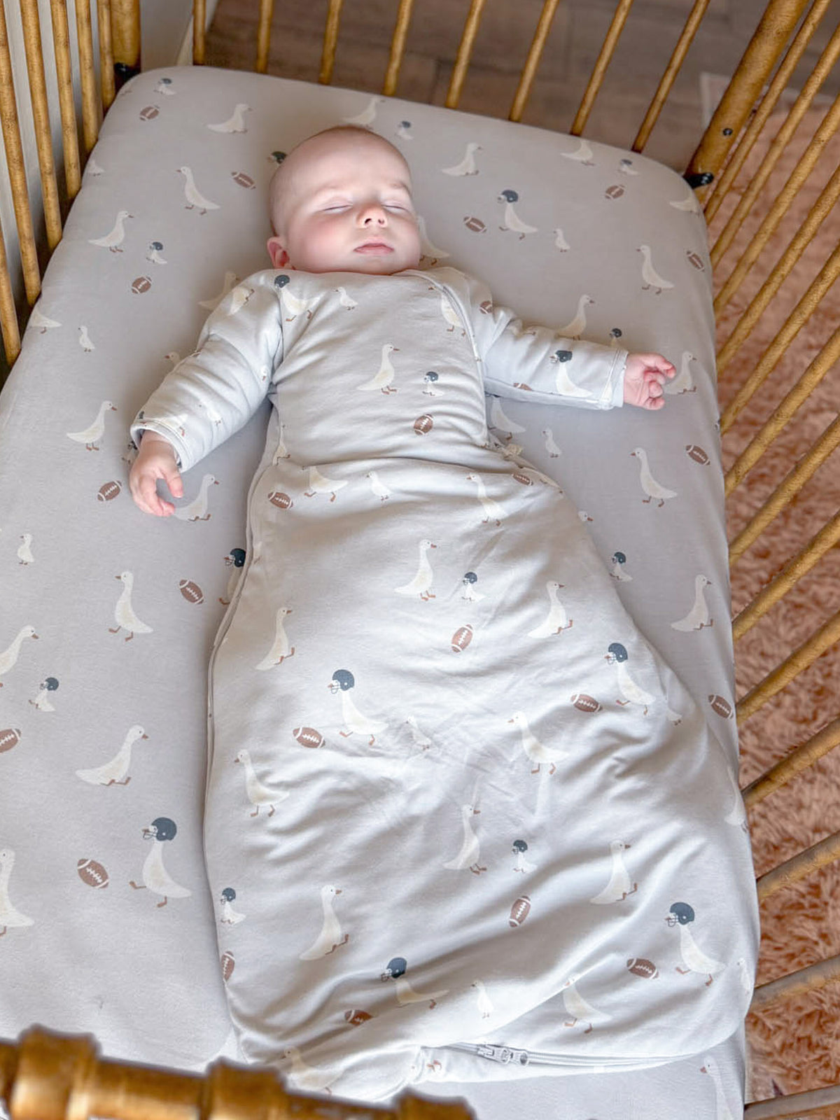 Light gray long-sleeve swaddle sack with bird-and-football print, sleeves for baby's arms
