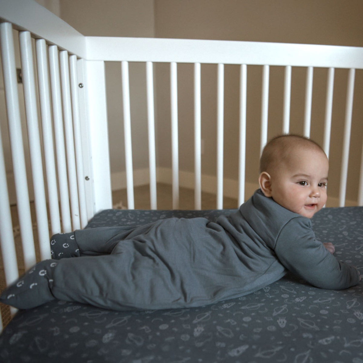 Gray footie sleep sack with long sleeves and zip-front, baby lying down.