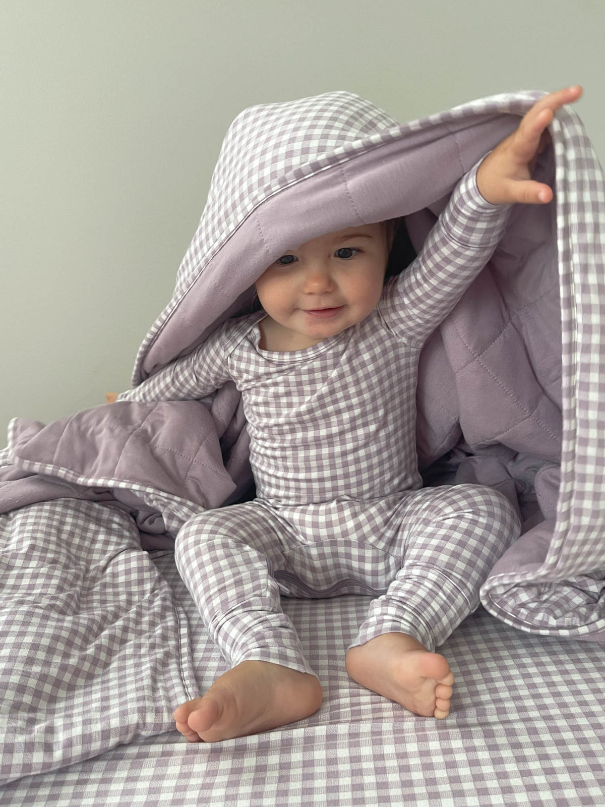 Hooded cloud blanket draped around toddler, lavender interior and gingham outer fabric