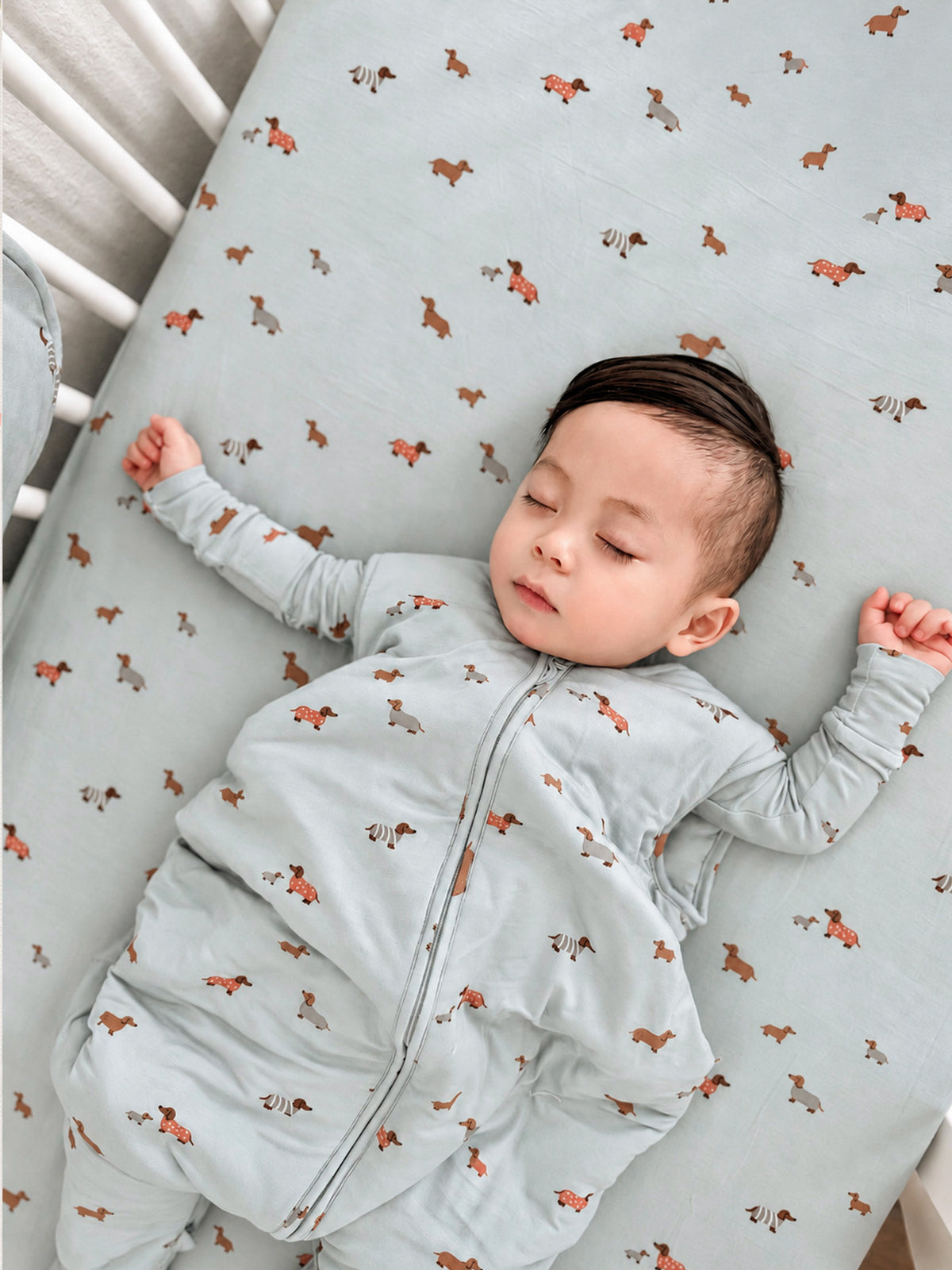 Light blue crib sheet with orange dog pattern, baby wearing light gray zip suit