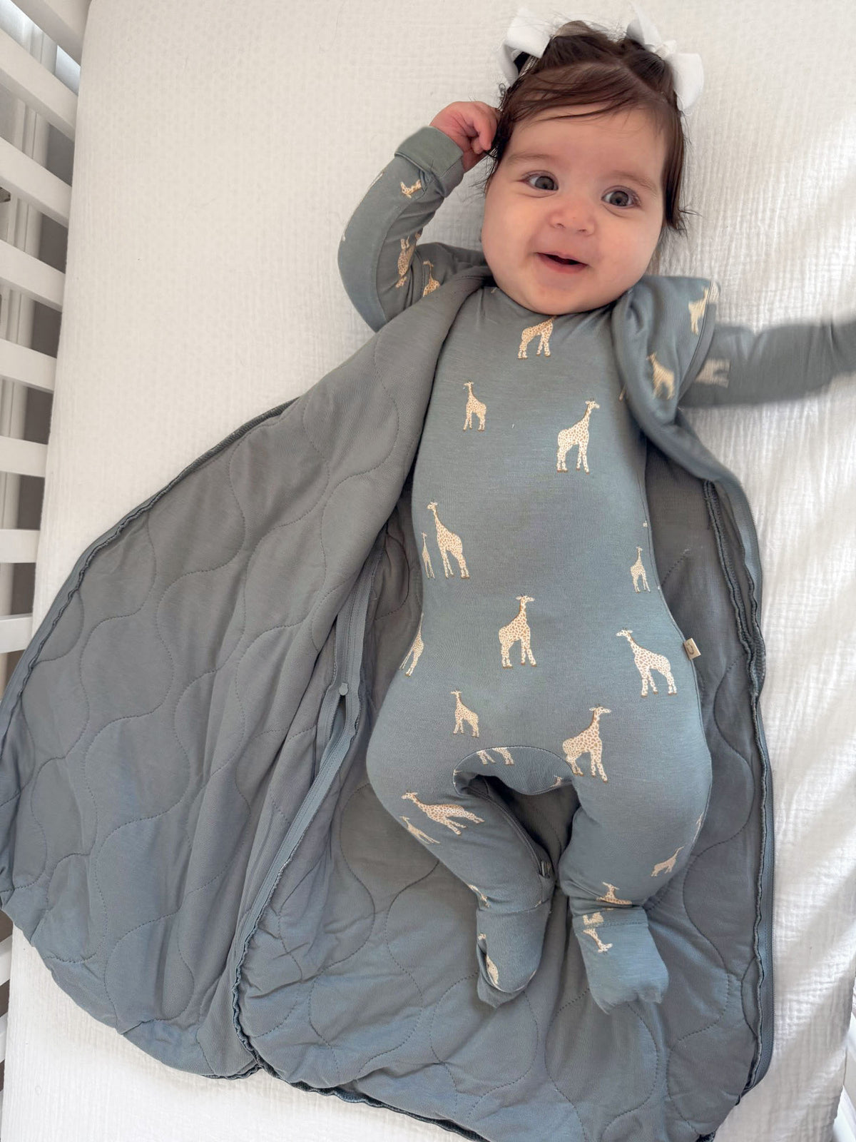 Blue-gray footed pajamas with beige giraffe print, baby wrapped in quilted blanket