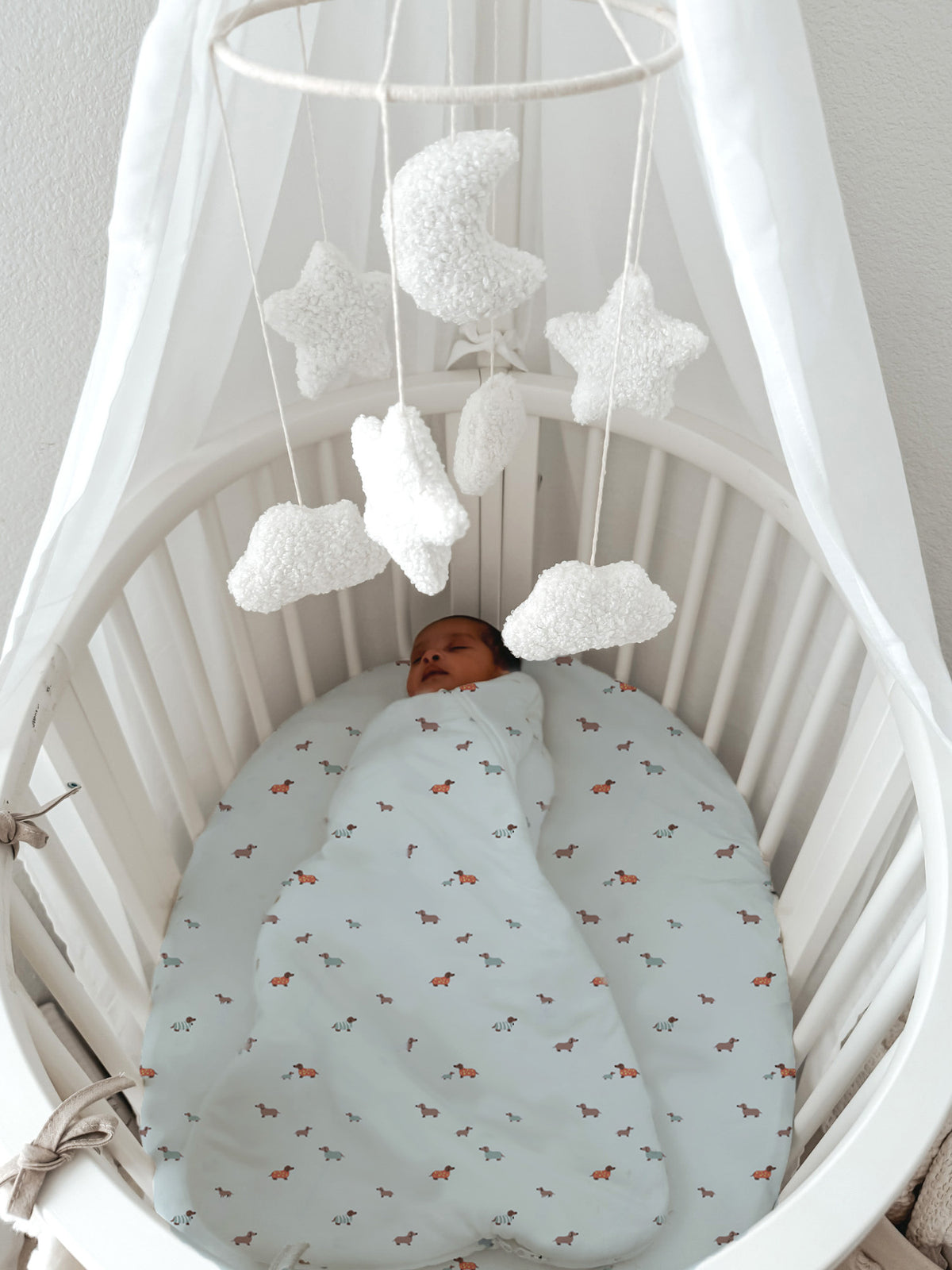 Light blue crib sheet with orange dog print pattern in white bassinet, baby sleeping