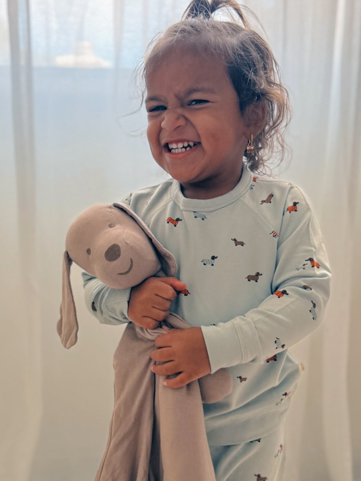 Baby laughing while hugging taupe puppy plush lovey with long floppy ears.