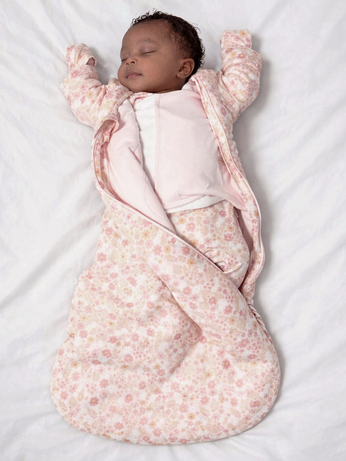 Floral long-sleeve swaddle sleep sack with wrap sides, soft pink and beige, baby upright.