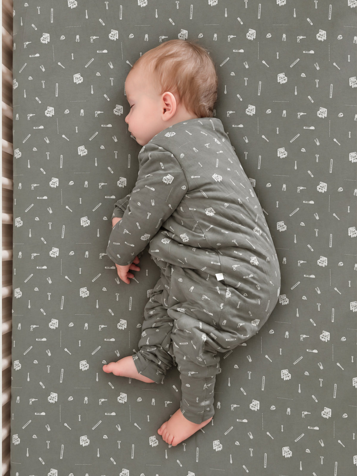 Grey crib sheet with white tool icons, baby resting on it